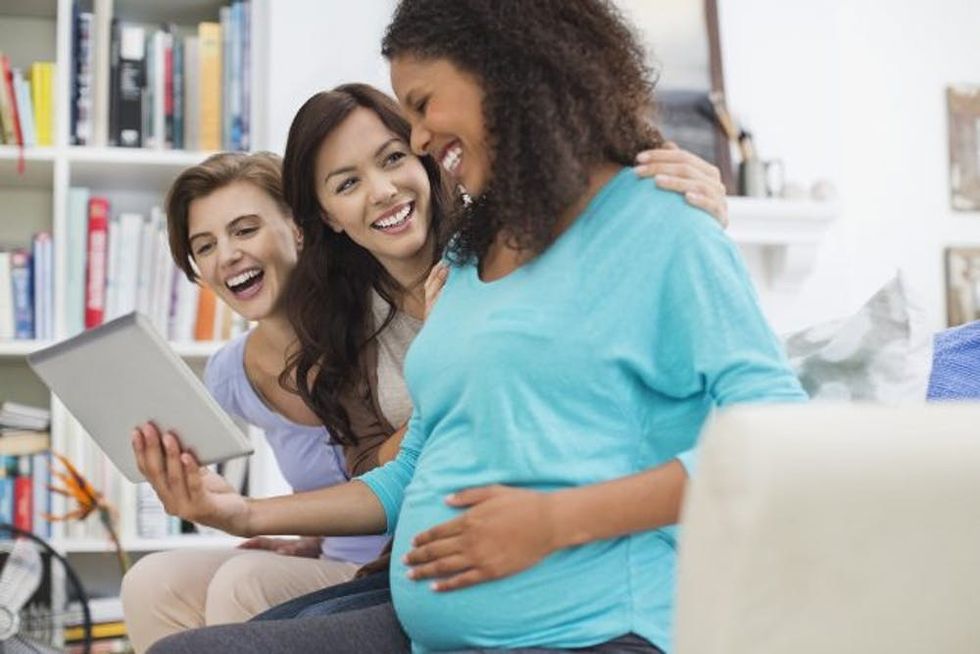 A pregnant woman and her partner laugh with another woman as they look at a tablet