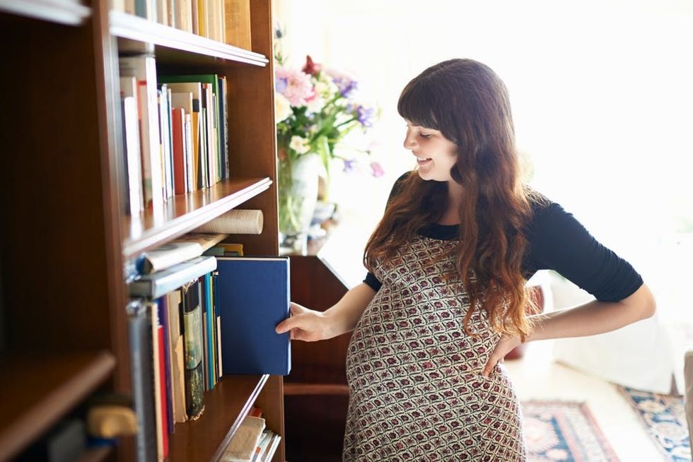 A pregnant woman browses a bookshelf
