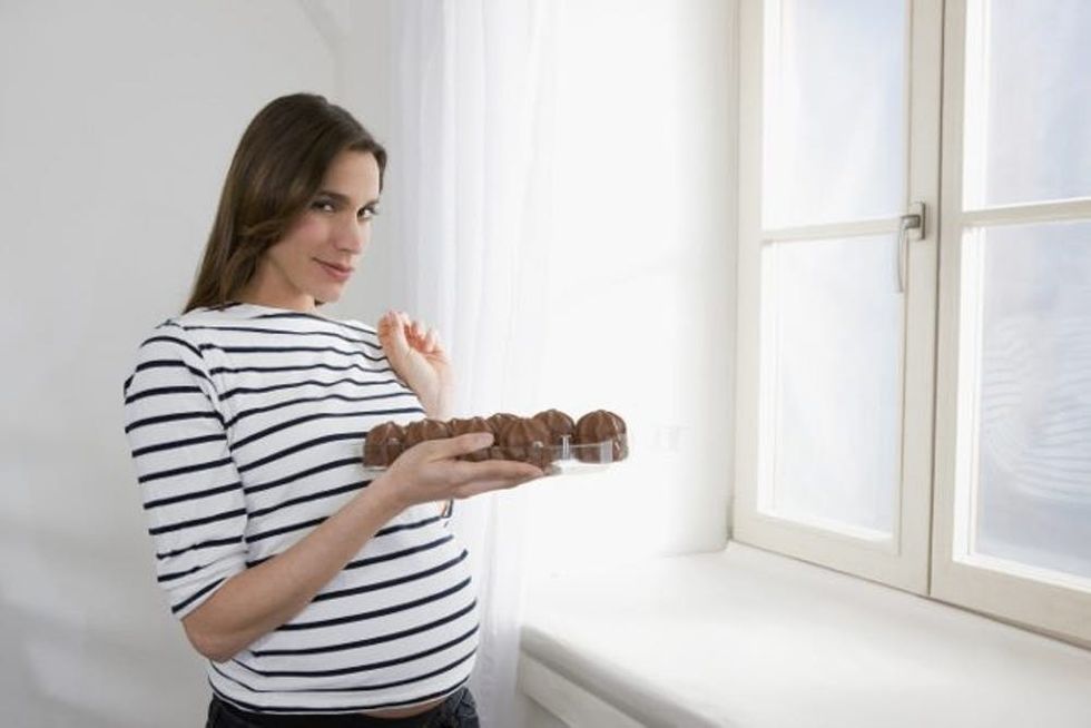 A pregnant woman considers a tray of cookies