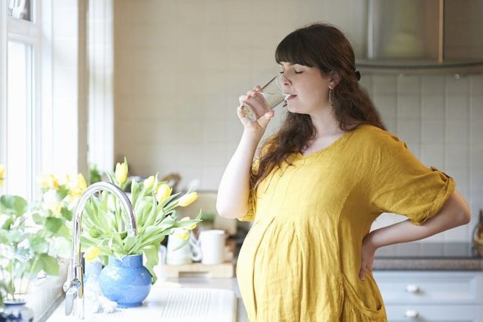 A pregnant woman drinks a glass of water in the kitchen