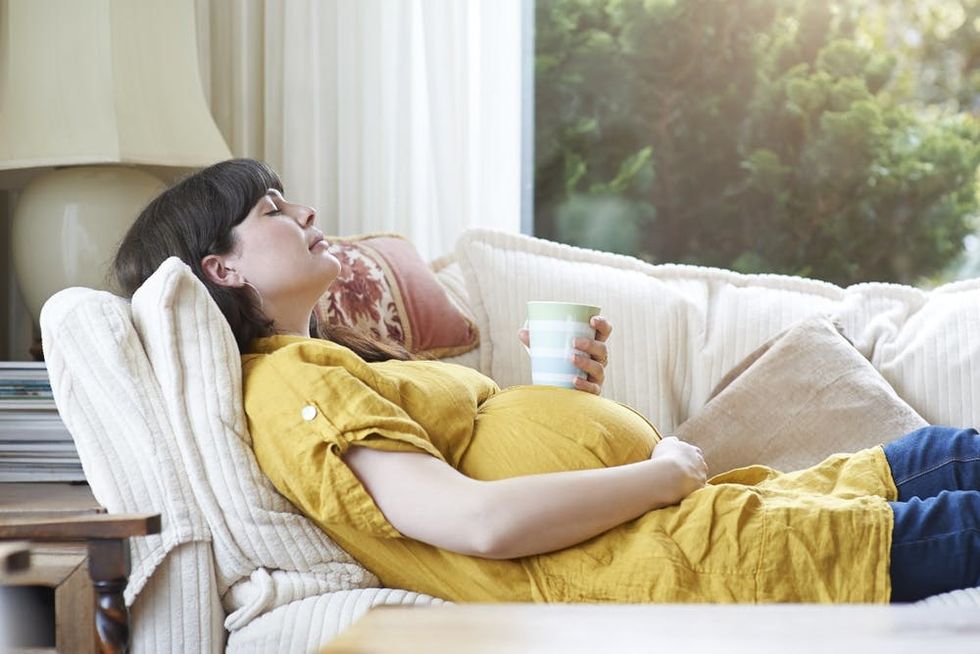 A pregnant woman relaxes on the sofa with a mug of hot tea