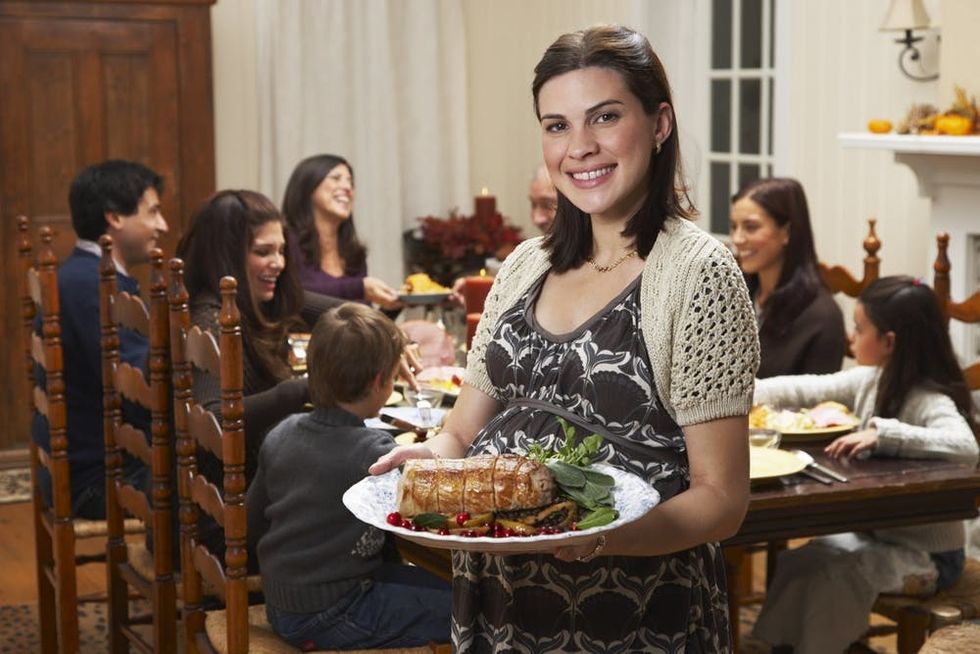 A pregnant woman serves a holiday dinner to her family