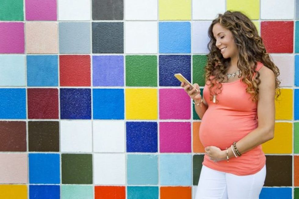 A pregnant woman smiles as she looks at her phone
