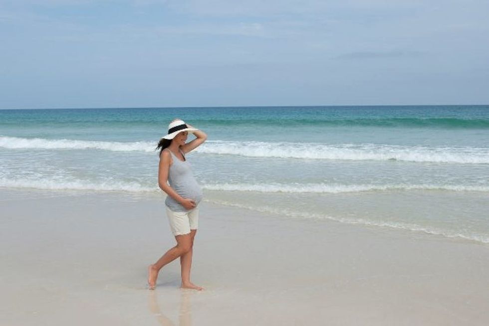 A pregnant woman strolls down a beach on a breezy day