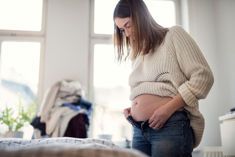 A pregnant woman struggles to button a pair of jeans