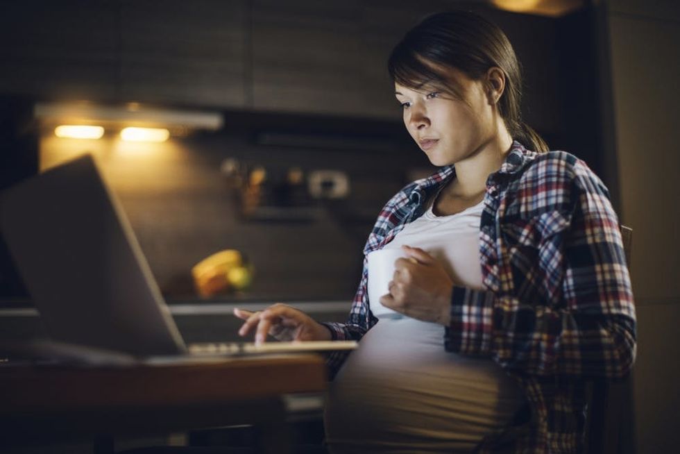 A pregnant woman uses a laptop in a darkened room