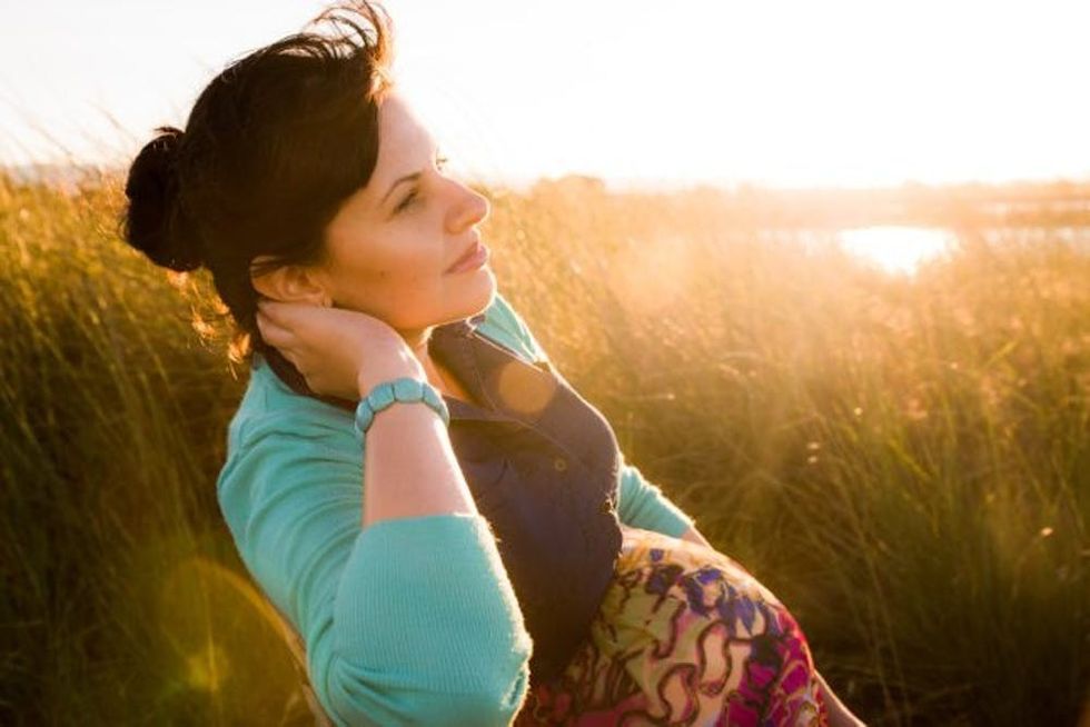 A pregnant woman watches a sunset over water