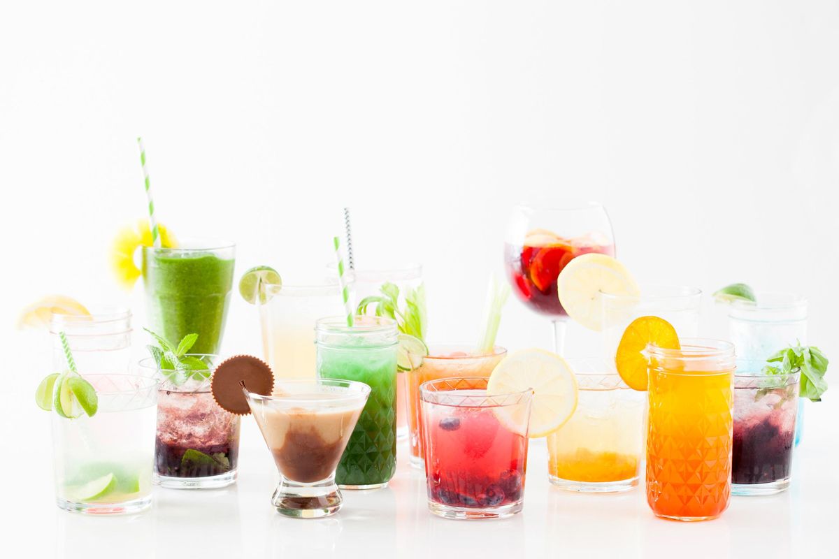 A rainbow display of various cocktail recipes with fruit and chocolate on a white counter with a white background