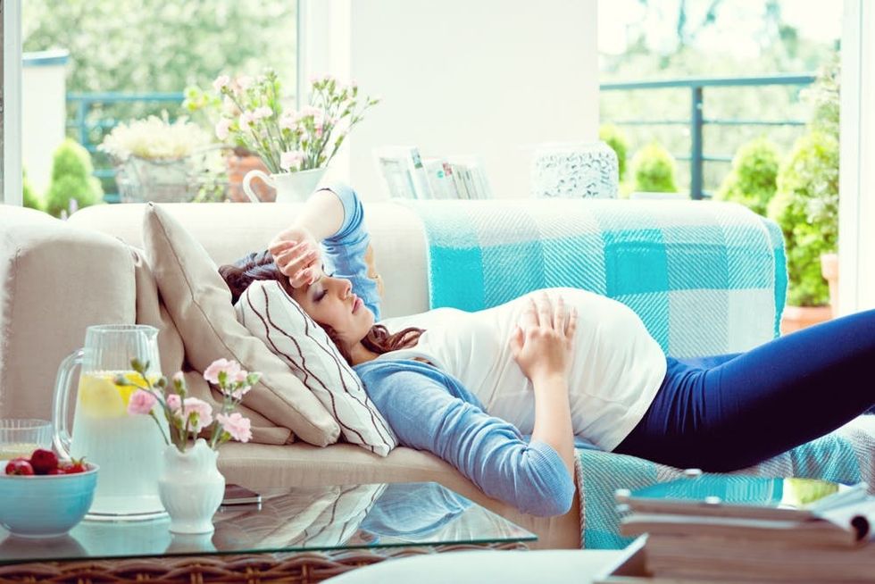 A sick pregnant woman rests on a couch