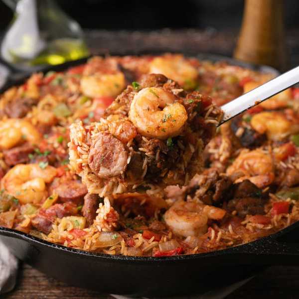 A skillet of jambalaya with shrimp, sausage, and vegetables, served with a ladle.