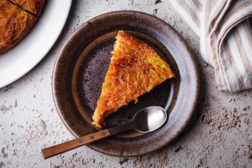 A slice of baked noodle kugel on a ceramic plate with a spoon.