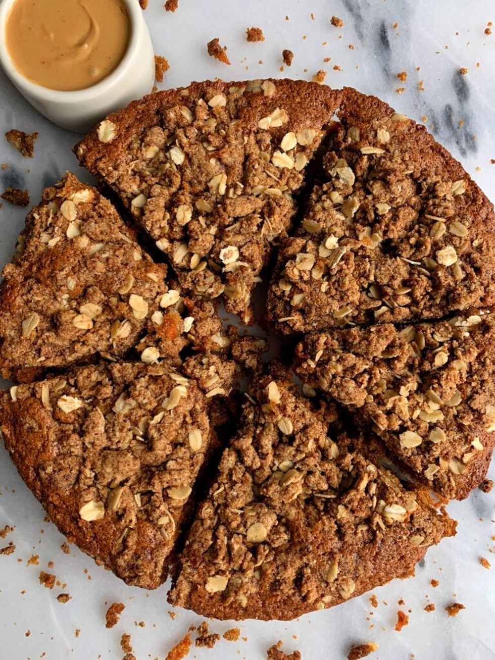 A sliced vegan carrot crumb cake sits on a marble surface next to a bowl of caramel.