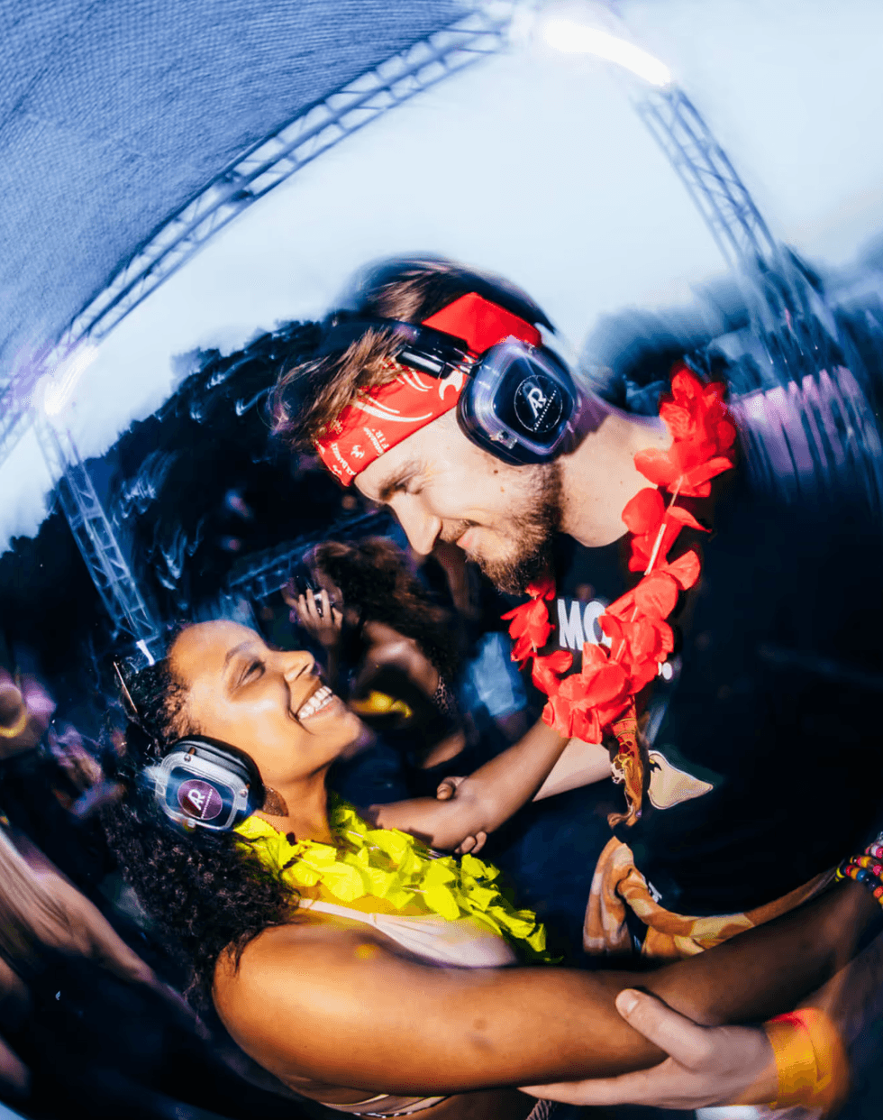 A smiling couple with headphones at a vibrant silent disco, wearing colorful leis.