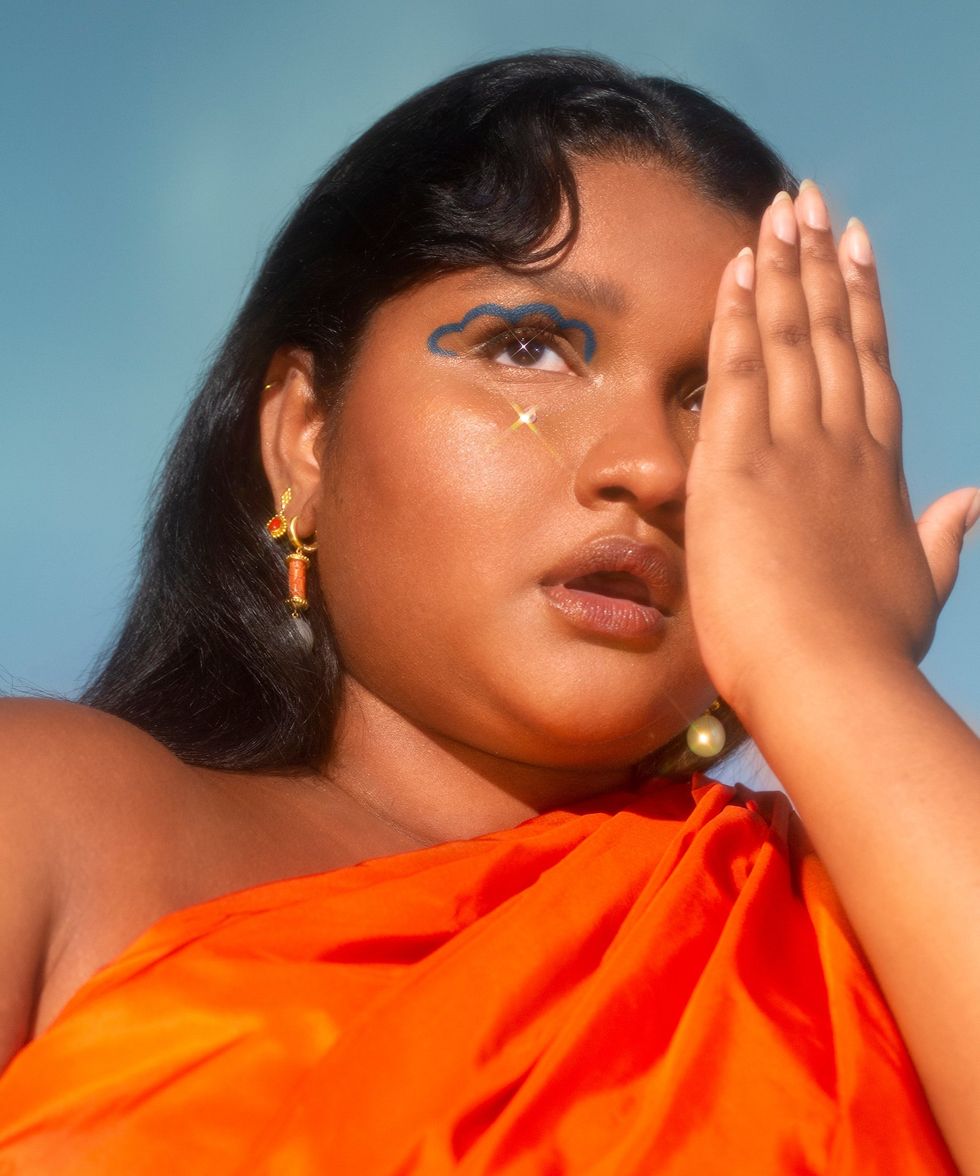 A South Asian woman stands with her one hand in front of one eye.