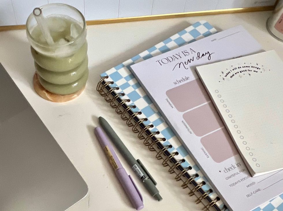 a stack of notebooks and planners next to an iced matcha latte and some pens