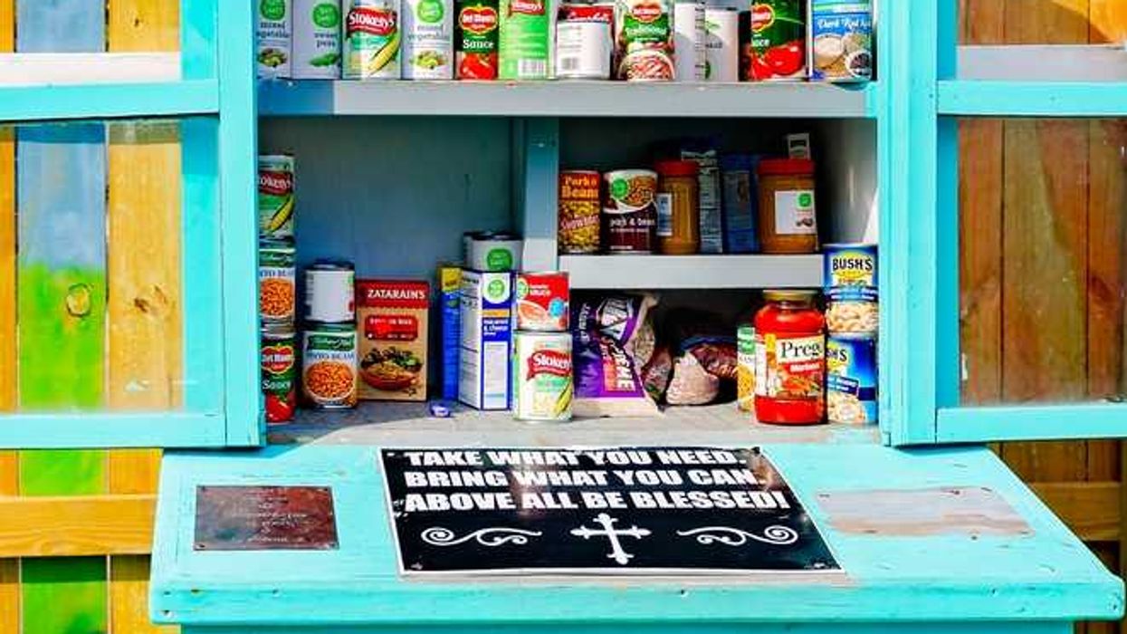 A teal food pantry stocked with canned goods and a sign: "Take what you need, bring what you can."