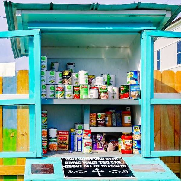 A teal food pantry stocked with canned goods and a sign: "Take what you need, bring what you can."