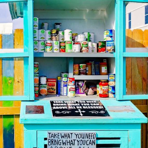 A teal food pantry stocked with canned goods and a sign: "Take what you need, bring what you can."