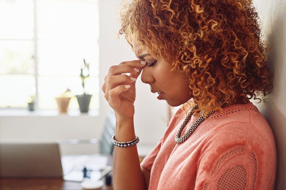A tired woman leans against a wall in her office