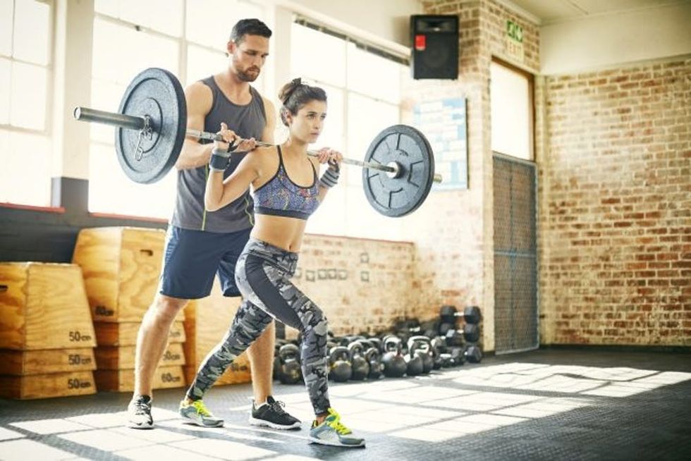 A trainer supervises as a woman lifts a barbell