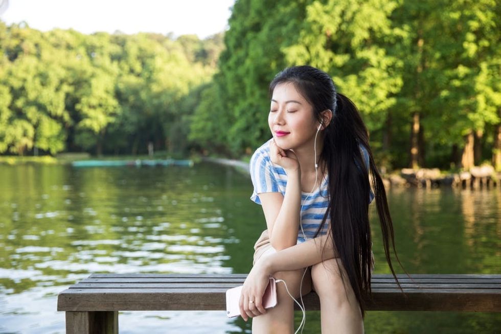 A woman closes her eyes to listen to music on a pier in front of a lake