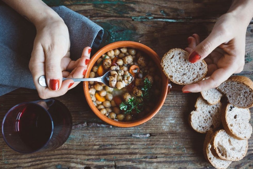 A woman eats a bowl of chickpea soup with bread