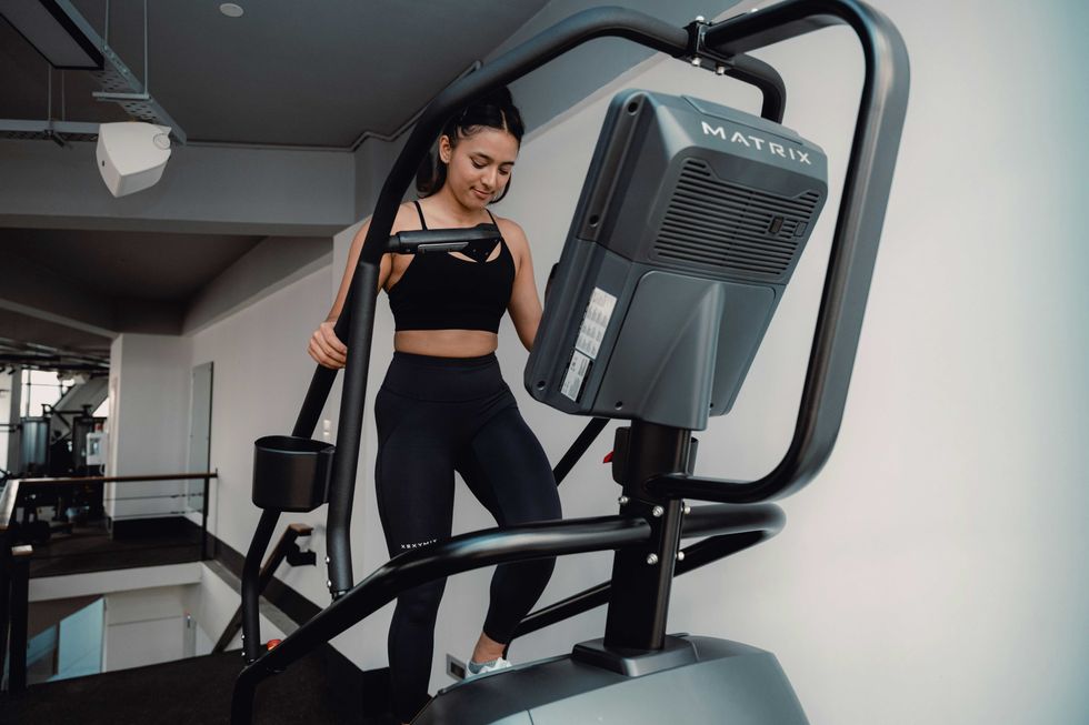 A woman exercises on a stair machine at the gym, wearing black workout clothes.