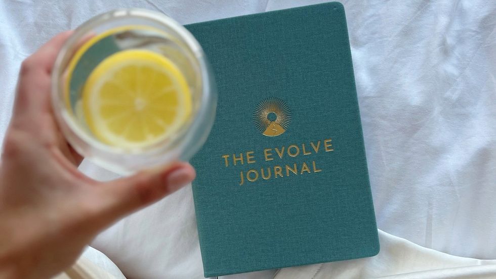 a woman holding a glass of water with lemon next to a journal
