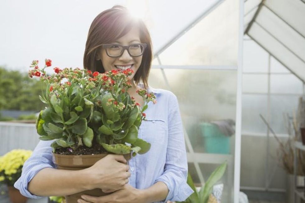 A woman holds a potted flower in a greenhouse