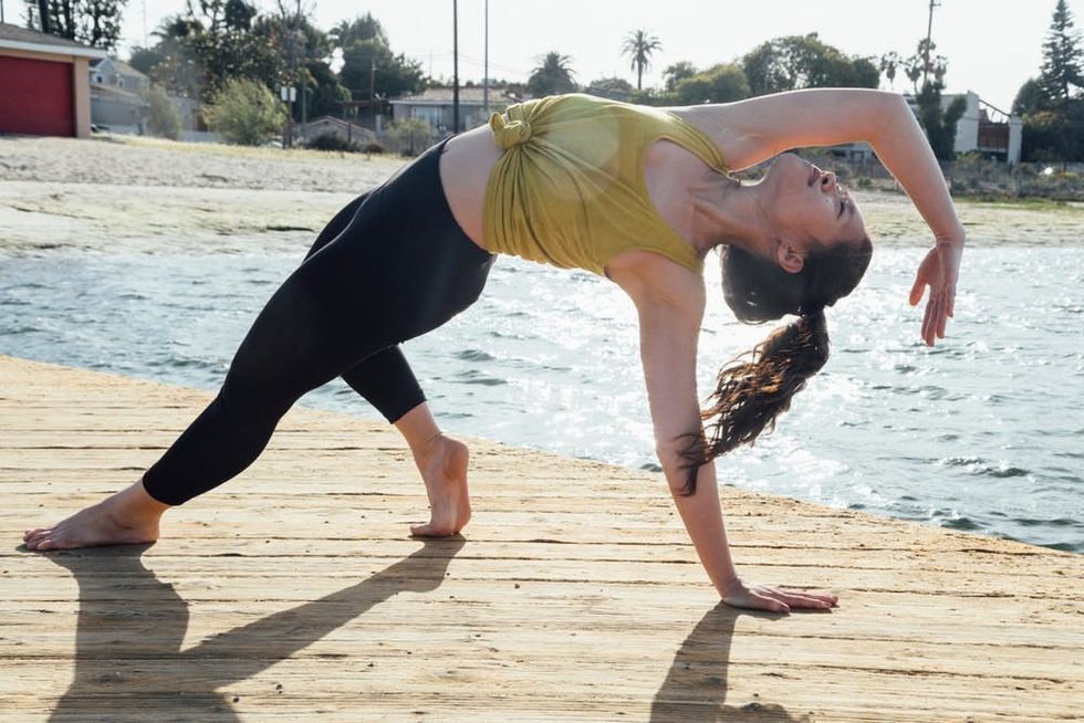 A woman holds a yoga pose on a beach boardwalk