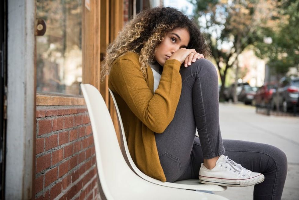 A woman hugs her knee as she sits outside a cafe
