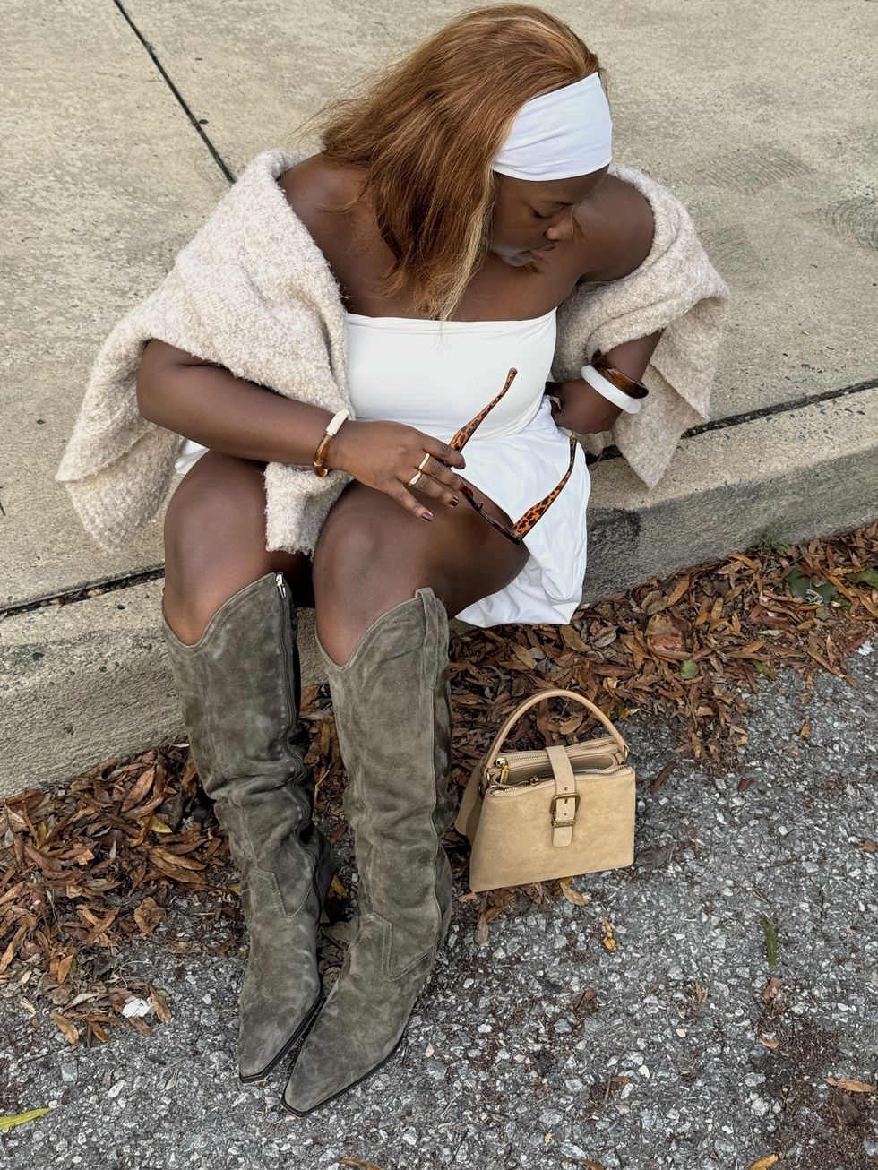a woman in a white dress with a sweater wrapped around her shoulders sitting on the sidewalk in the fall