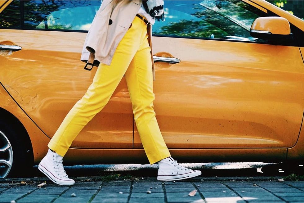 A woman in bright yellow pants walks past an orange car