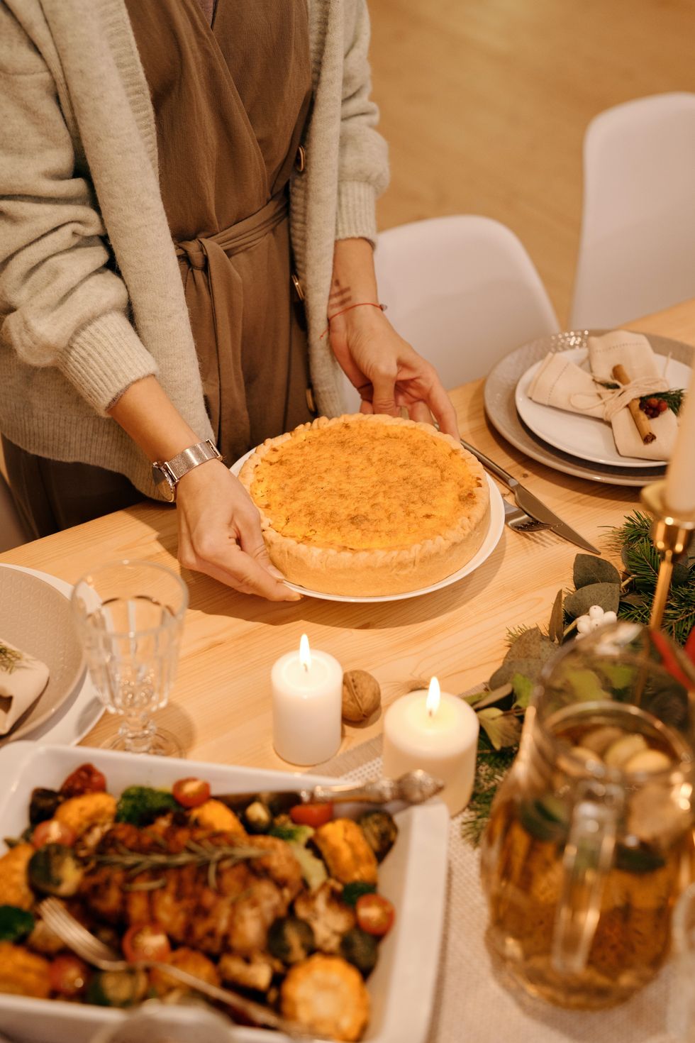 A woman is putting out a cake on to an existing Thanksgiving spread.