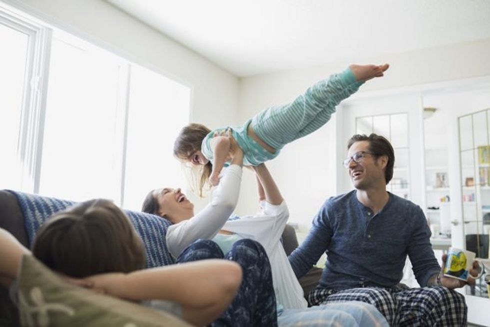 A woman laughs with her family as she lifts her daughter over her head