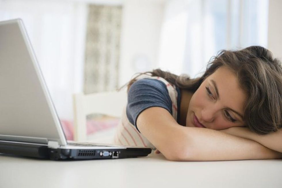 A woman lays her head on a desk as she looks at her laptop