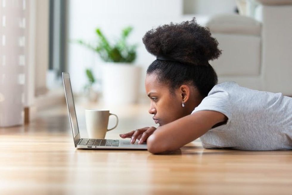A woman lays on the floor with her laptop and a cup of coffee