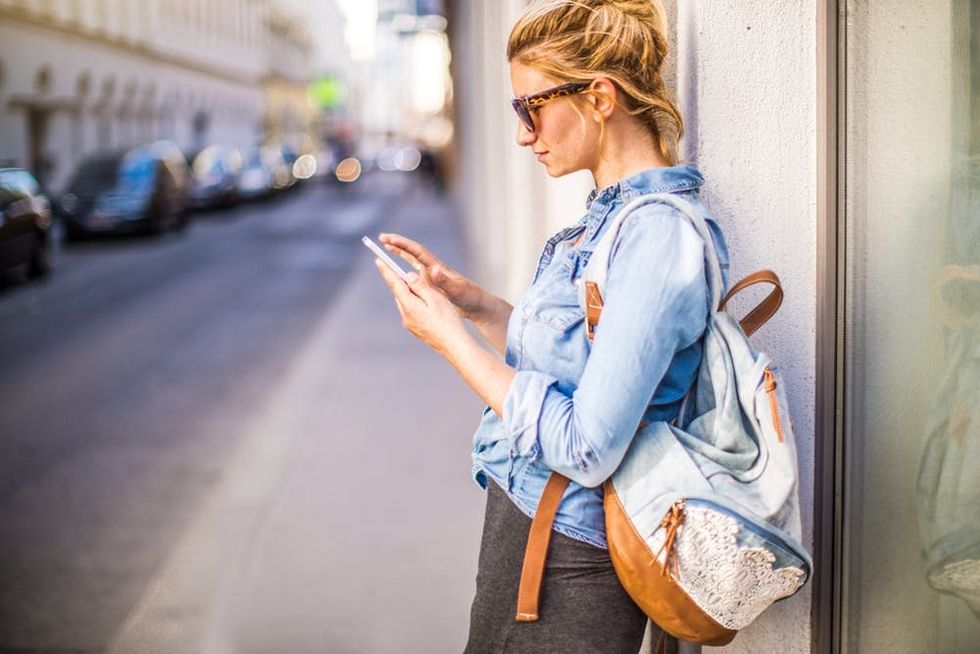A woman leans against a building as she sends a text