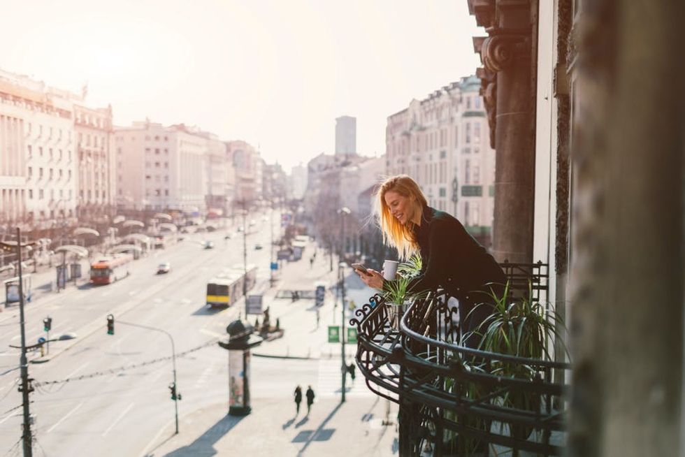 A woman leans on a balcony overlooking a bustling city