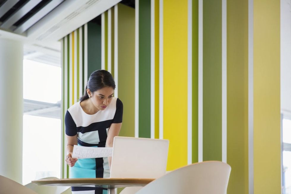 A woman leans over a laptop to work