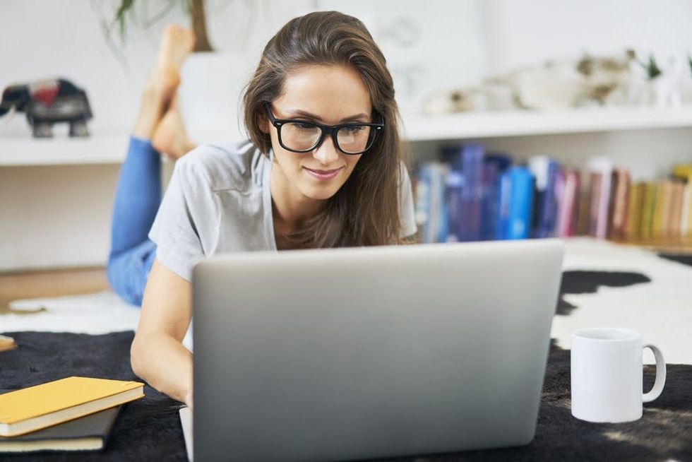 A woman lies on a rug using a laptop