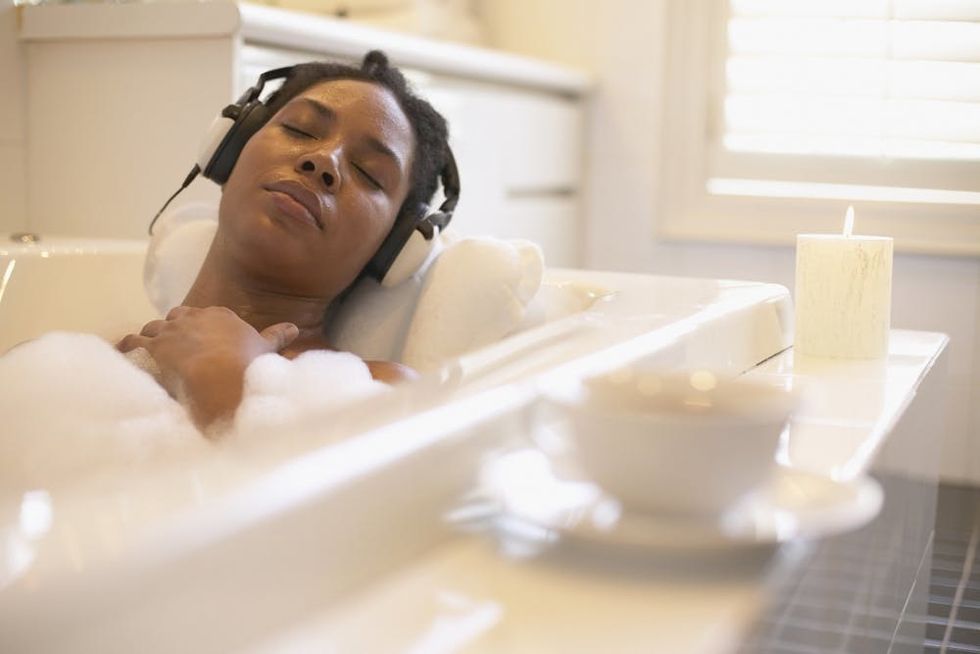 A woman listens to headphones while taking a bubble bath