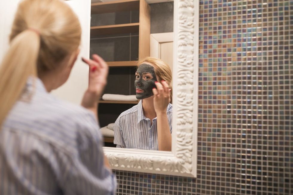 A woman looks in the mirror to apply a facial mask