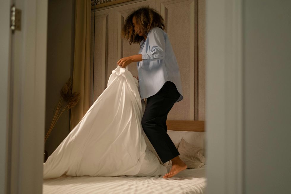 a woman making the bed with her bed sheets