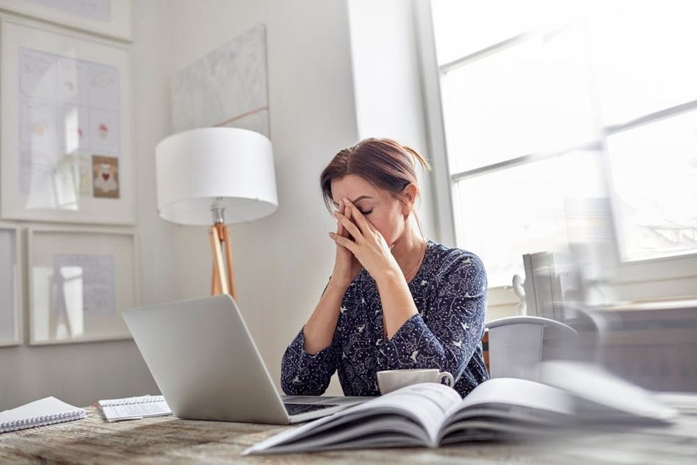 A woman rests her face in her hands at a desk covered in work