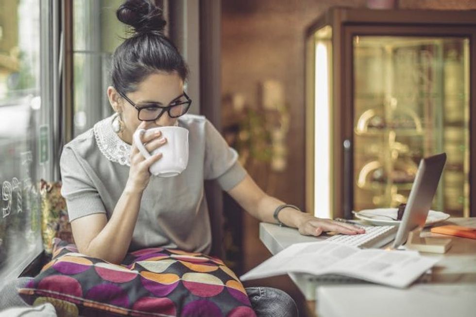 A woman sips from a mug as she works on a laptop