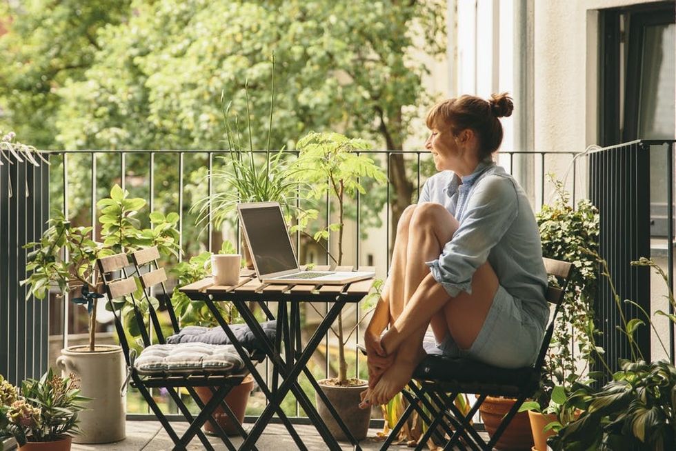 A woman sits at a table on a balcony surrounded by greenery
