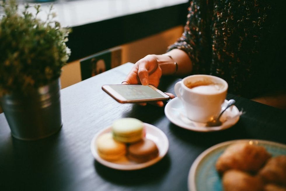 A woman sits in a cafe with a drink and a plate of macarons