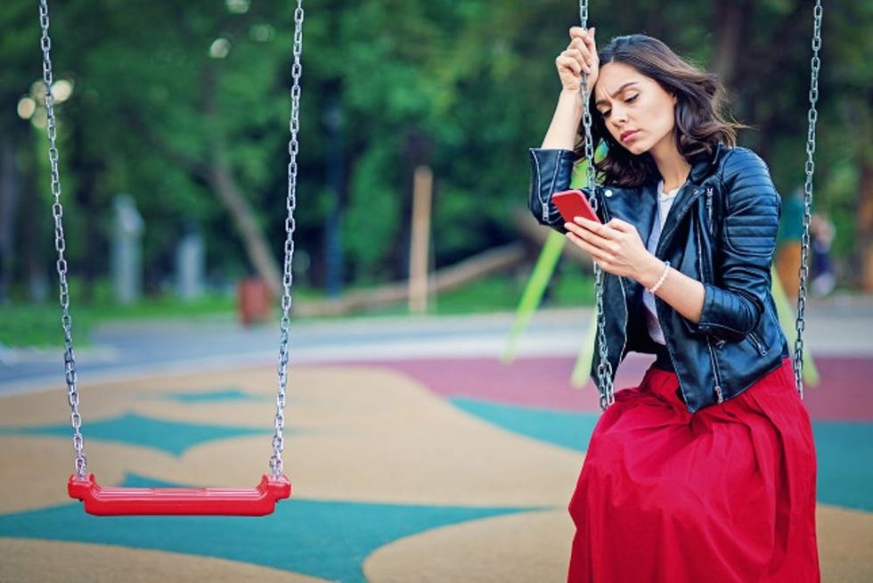 A woman sits on a swing as she sadly reads her phone