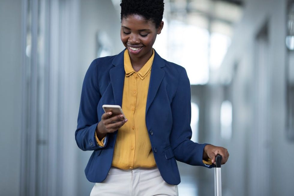 A woman smiles as she looks down at her phone while walking down an office hallway